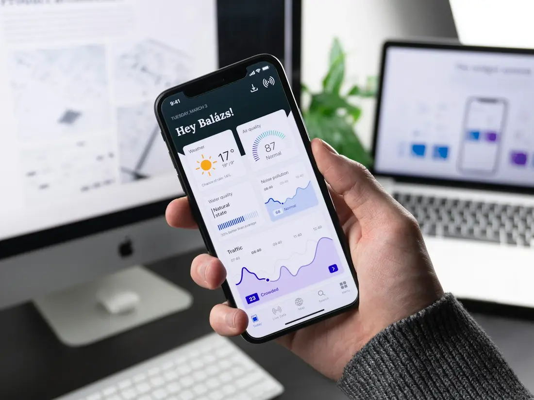 Mano sosteniendo un teléfono con una app frente a una computadora
